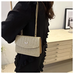 Detail of beige straw crossbody bag featuring V-weave pattern and white butterfly clasp