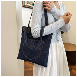 Detail of navy blue denim tote bag with brown leather accent and contrast stitching details