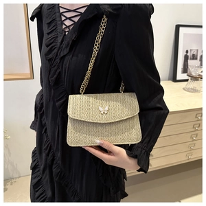 Detail of straw woven bag featuring delicate white butterfly accents and gold chain strap