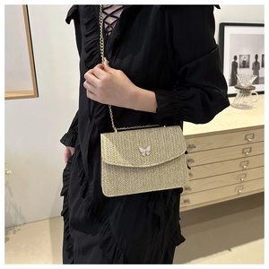 Detail of beige straw crossbody bag with white butterfly motif and gold chain strap