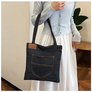 Close-up of deep blue denim tote bag with orange contrast stitching and leather patch