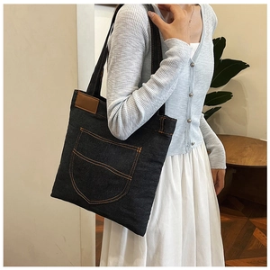 Close-up of black denim shoulder bag with orange contrast stitching and brown leather patch