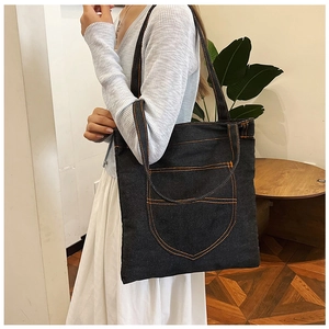 Detail of dark denim tote bag featuring orange contrast stitching and large front pocket