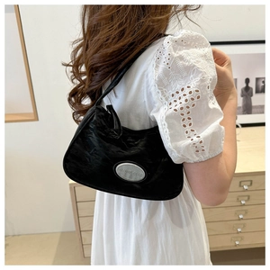 Detail of black pleated shoulder bag with oval silver metal logo and velvet texture