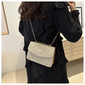 Detail of a straw woven crossbody bag featuring a golden chain strap and a white butterfly charm