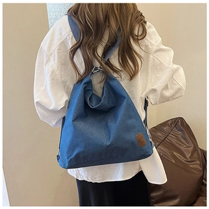 Detail of blue denim backpack showing rich twill texture and brown leather patch logo