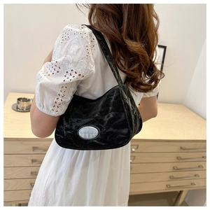Close-up of black wrinkled texture shoulder bag with oval silver metal logo plaque