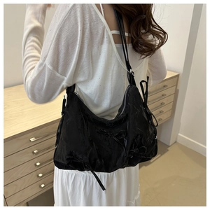 Detail der schwarzen Hobo-Tasche mit Schleifen und verstellbarem Gurt auf weißem Outfit