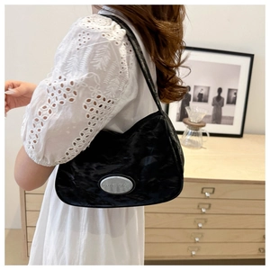 Detail of black underarm bag featuring glossy pleated texture and silver oval logo plaque