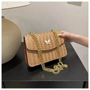 Close-up of straw woven crossbody bag with golden chain strap and white butterfly buckle