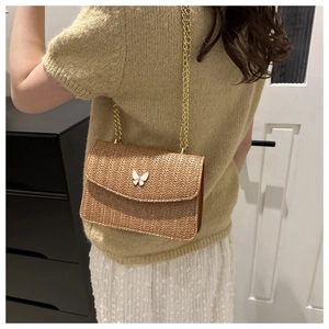 Detail of straw woven crossbody bag with gold chain and butterfly buckle decoration