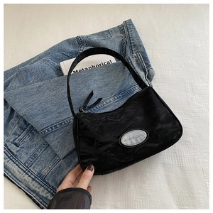 Detail of black pleated crescent underarm bag with silver logo plate on white background