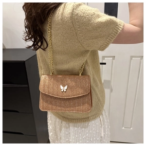 Detail of tan woven straw shoulder bag with white butterfly clasp and gold chain strap