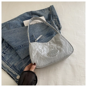 Detail shot of the pleated silver texture and oval metal logo on this stylish shoulder bag