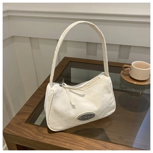 Close-up of white underarm bag featuring textured fabric and silver GYNS ONE metal plate