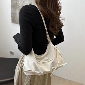 Cremeweiße Schultertasche mit Schleifen-Details und Textur, am Modell getragen