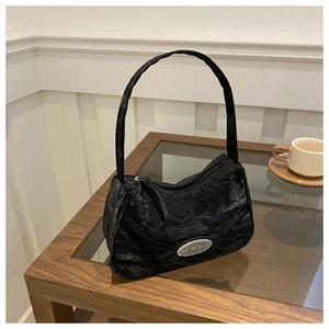 Detail view of black underarm bag featuring pleated texture and silver brand logo plate