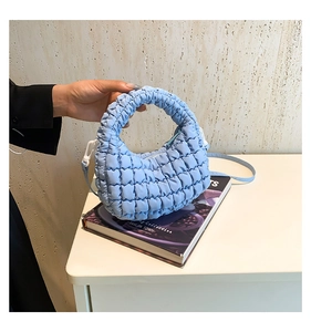Detail of light blue quilted nylon tote bag showing textured puffy fabric and side buckle