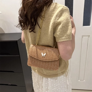 Brown woven straw crossbody bag with white butterfly clasp and gold chain strap