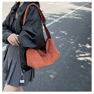Street style shot of an orange quilted dumpling bag with white geometric stitching details