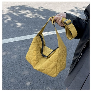 Detail of yellow quilted dumpling bag with adjustable strap worn by model outdoors