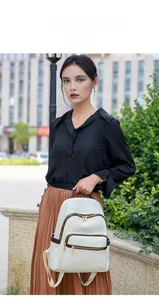 Detailed view of white woven leather backpack with brown trim and gold zippers in street setting