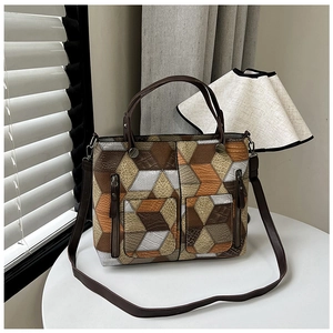 Detailed shot of a geometric patchwork tote bag with side zippers on a white table