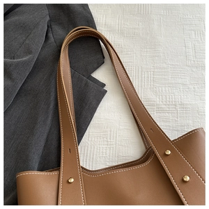 Detail einer braunen Leder-Tragetasche mit Kontrastnähten und goldfarbenen Nieten