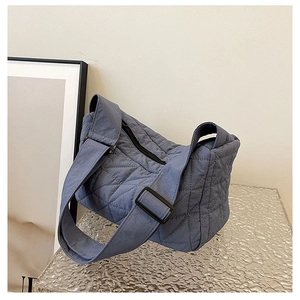 Detail of blue quilted dumpling bag with adjustable strap on a glass pedestal