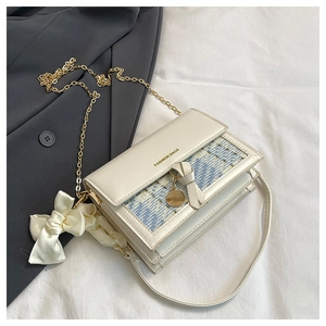 Detail of tweed crossbody bag with gold chain strap and silk scarf on a grey blazer