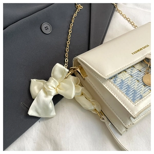 Detail of cream flap bag featuring light blue tweed fabric, gold chain and silk bow