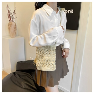 Detail of woven straw crossbody bag featuring cutout patterns and tassel accents