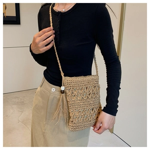 Detail of hand-woven hollow straw crossbody bag with side tassels and wooden beads
