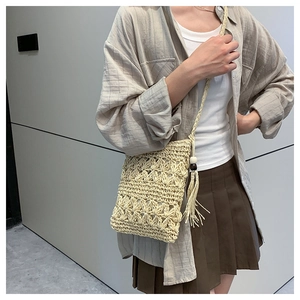 Détail du sac en paille beige avec motif floral évidé et pompons à franges décoratifs