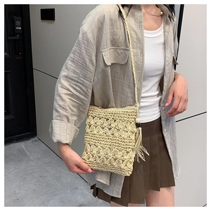 Détail du sac à bandoulière en paille tissée avec motif ajouré et pompon en perles de bois