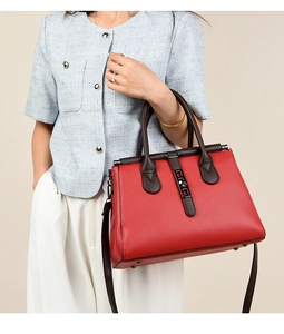 Detail of red pebbled leather handbag with brown straps and metal twist lock