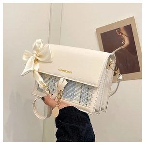 Detailed close-up of a white tweed chain bag with silk bow and fashion bags lettering