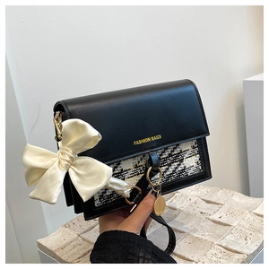 Close-up of black leather bag with tweed panel and white satin bow decorative charm