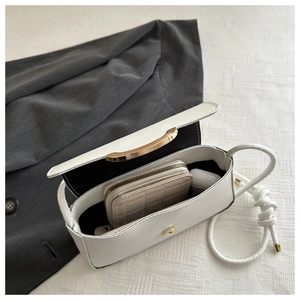 Detailed interior of a white leather underarm bag with gold handle and knotted strap
