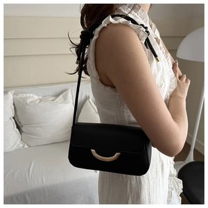 Detail of minimalist black leather underarm bag with gold metal buckle on model