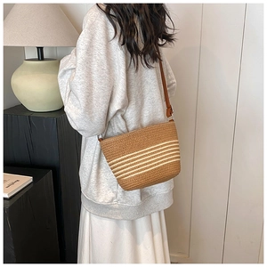 Close-up of woven straw shoulder bag with white stripes on a model in a modern home setting