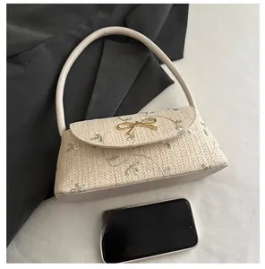 Beige woven baguette bag with floral embroidery and golden bow buckle next to a smartphone