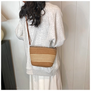 Detail of hand-woven straw crossbody bag with dark brown textures and white stripe