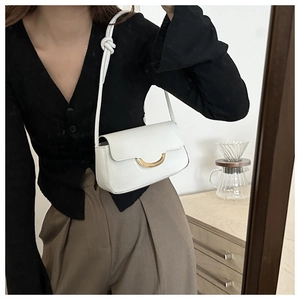 Close-up of white leather underarm bag featuring a gold crescent buckle and knot strap detail
