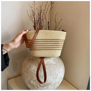 Detailed view of hand-woven straw bucket bag with brown leather strap and rustic texture