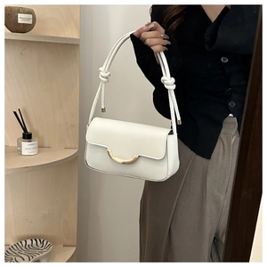 Close-up of white glossy leather shoulder bag with gold crescent buckle and knotted strap