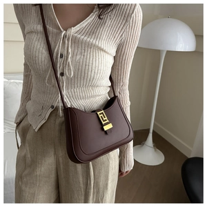 Détail d'un sac demi-lune marron foncé avec boucle dorée porté par un mannequin chic