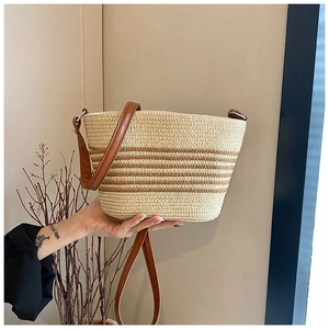 Detail of woven straw bucket bag with brown leather strap and summer stripe patterns