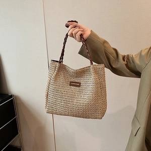 Détail du sac cabas en paille tissée avec écusson en cuir brun et anses en corde