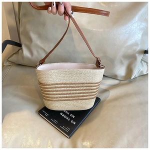 Macro view of woven straw bucket bag with brown stripes and adjustable leather strap